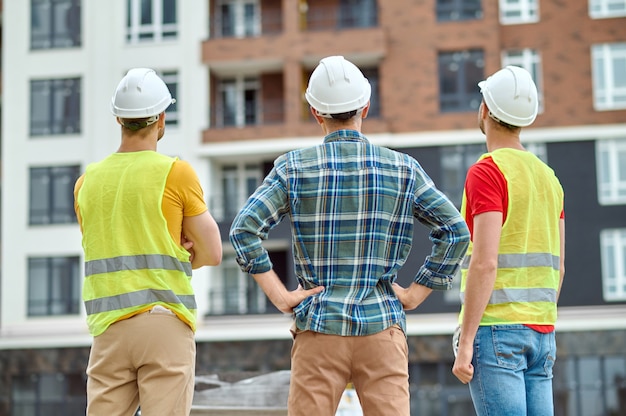 Trzech robotników w kaskach stojących przed nowym budynkiem