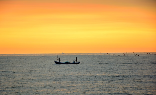 Trzech rybaków na małej łodzi rybackiej wyjść na ryby o zachodzie słońca.