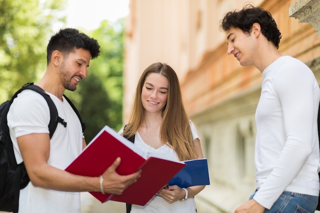 Trzech studentów rozmawiających ze sobą na dziedzińcu uczelni