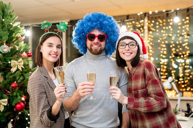 Trzech szczęśliwych młodych kolegów opiekania szampanem na Boże Narodzenie, ciesząc się imprezą w biurze
