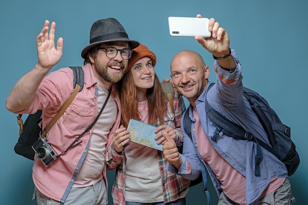 Trzech szczęśliwych przyjaciół turystów z plecakami podróżuje i robi zdjęcia smartfonem