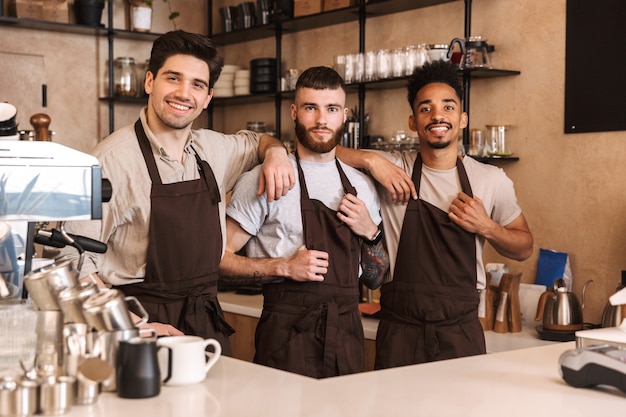 Trzech wesołych męskich baristów stojących przy ladzie kawiarni w pomieszczeniu