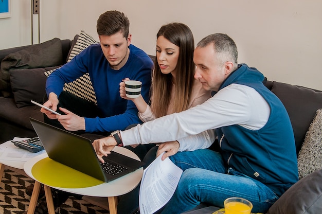 Trzej młodzi ludzie pracują razem nad nowym projektem. Koncepcja uruchomienia. Zespół szczęśliwych pracowników Urzędu pracy na komputerze przenośnym, uśmiecha się.