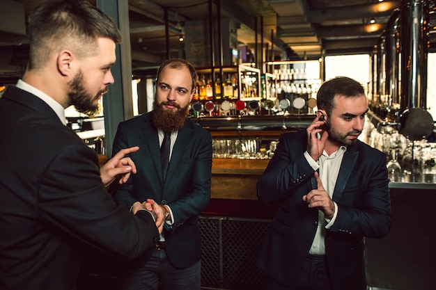 Trzej młodzi mężczyźni stoją w pubie. Jedną ręką trzymaj słuchawki. Pokazuje palec w górę. Drugi młody człowiek patrzy na początku i próbuje porozmawiać. Trzeci facet patrzy na drugi.