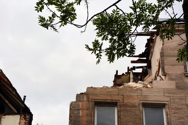 Trzęsienie ziemi uszkodziło ścianę budynku mieszkalnego z oknami i gałęzią drzewa na tle nieba