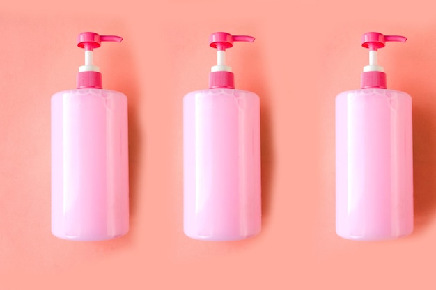 Trzy butelki z różowym płynem do zmywania naczyń na różowym tle Minimalna koncepcja
