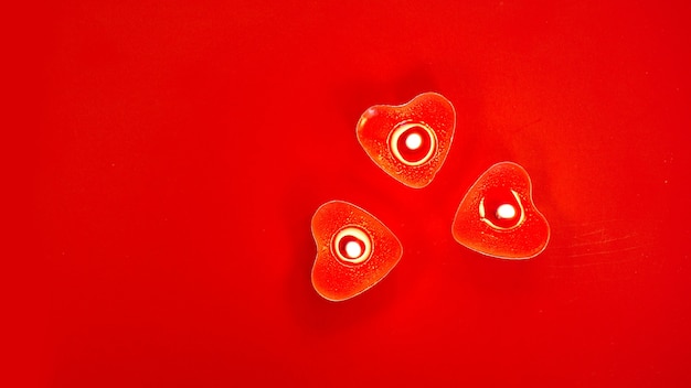 Trzy czerwone płonące świece z dekoracjami w kształcie serca na czerwonym tle. Walentynki.
