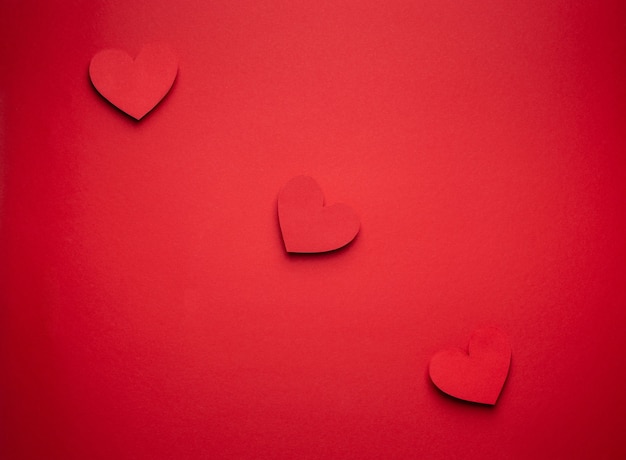 Trzy czerwone serca z rzędu wycięte z papieru na czerwonym tle, rzemieślnicze w stylu origami, z góry. Koncepcja miłości monochromatyczne czerwony romantyczny Walentynki. Różnej wielkości serca widok z góry, projekt papieru artystycznego