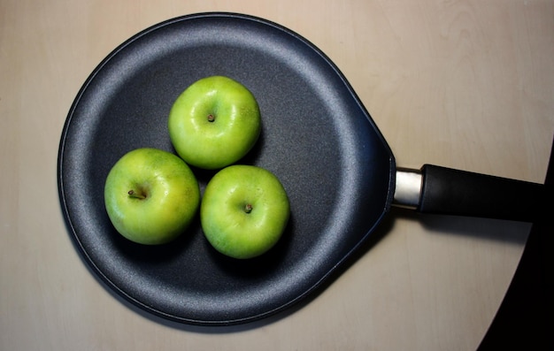 Trzy dojrzałe zielone soczyste jabłka na patelni na drewnianym stole