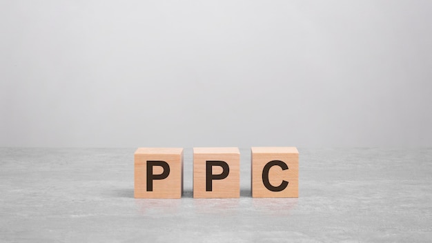 Trzy drewniane klocki z literami PPC na jasnoszarej koncepcji biznesowej stołu PPC, skrót od Pay Per Click