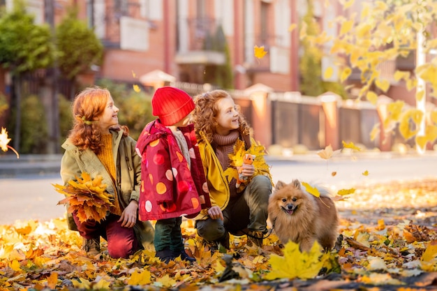 Trzy dziewczynki, dwie starsze siostry i dziecko spacerują z puszystym pomorskim psem ulicą i patrzą na opadłe liście w słoneczny jesienny dzień