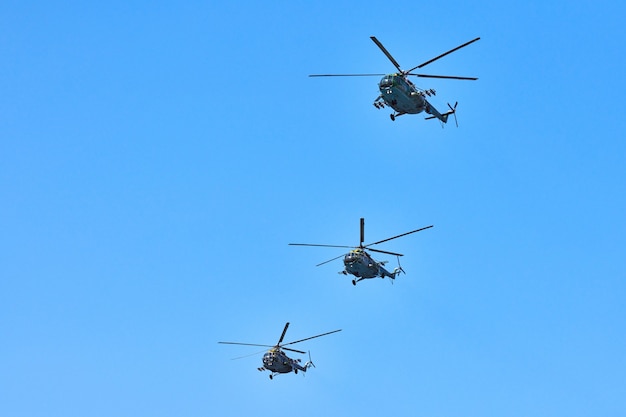 Trzy helikoptery wojskowe lecące w błękitne niebo podczas wykonywania lotu demonstracyjnego, skopiuj przestrzeń. Zespół akrobacyjny wykonuje lot na pokazach lotniczych