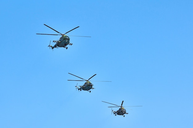 Trzy helikoptery wojskowe lecące w błękitne niebo podczas wykonywania lotu demonstracyjnego, skopiuj przestrzeń. Zespół akrobacyjny wykonuje lot na pokazie lotniczym