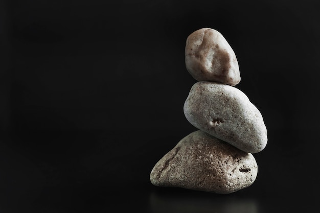 Trzy kamienie stoją jeden na drugim, utrzymując równowagę. Ciemne tło. Skopiuj miejsce...