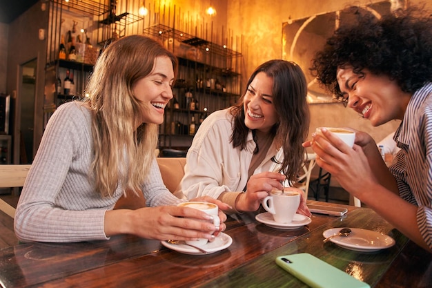 Trzy kobiety pijące kawę siedzące przy stole w kawiarni. Grupa przyjaciół pije cappuccino w barze.