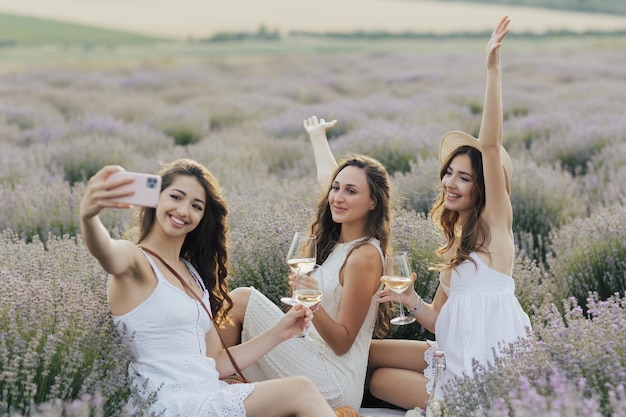 Trzy kobiety siedzące na polu lawendy i robiące selfie