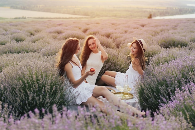 Trzy kobiety w białych sukniach siedzą na polu lawendy