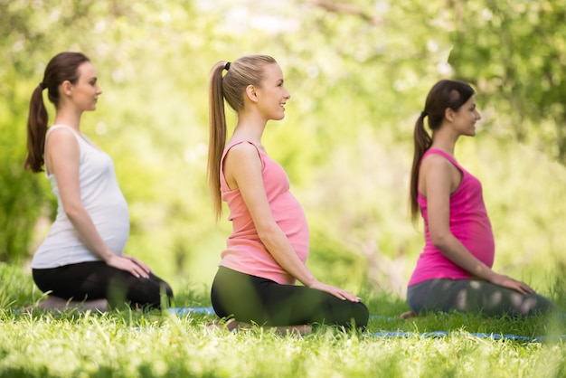 Trzy kobiety w ciąży relaksuje na trawie outdoors.