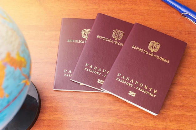Trzy kolumbijskie paszporty rozłożone obok globusa i długopisu na drewnianym biurku