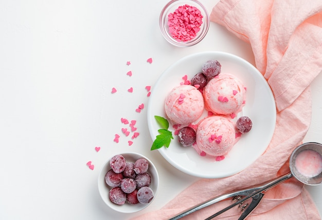 Trzy kulki lodów jagodowych z mrożonymi wiśniami na białej ścianie z różową serwetką. Widok z góry, kopia przestrzeń. Letni deser.