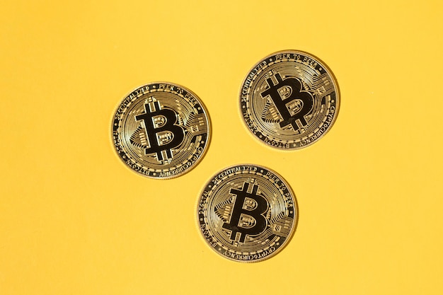 Trzy monety Bitcoin na żółtym tle. Pojęcie kryptowaluty, oszczędności i oszczędności.