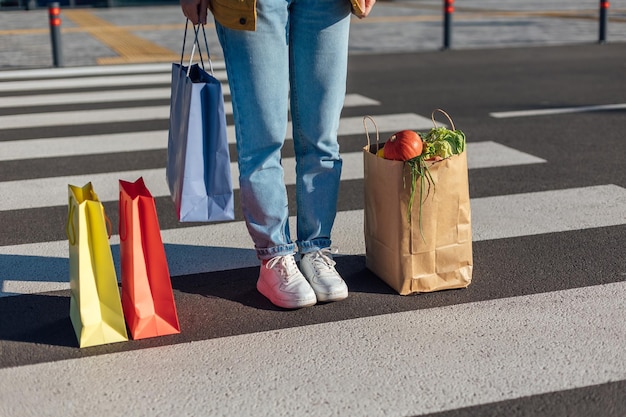 Trzy papierowe torby na zakupy i kobieta stojąca na oznaczonym przejściu dla pieszych