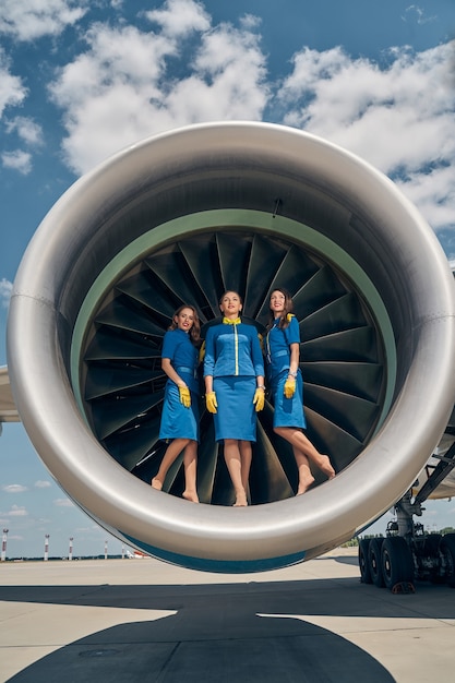 trzy piękne kaukaskie stewardesy w skórzanych rękawiczkach stoją w silniku odrzutowym