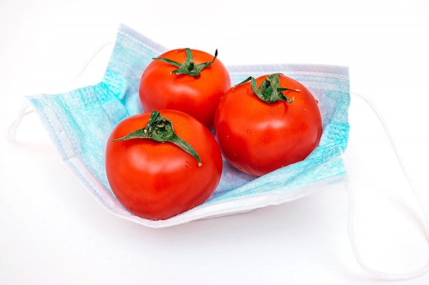 Trzy pomidory leżą na ochronnej masce medycznej. Kryzys rolny związany z pandemią koronawirusa.