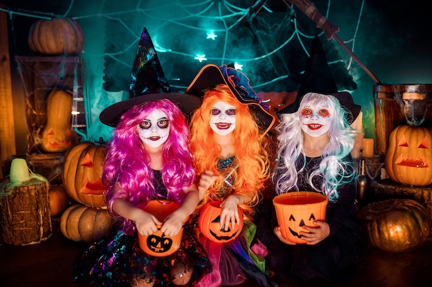 Trzy słodkie śmieszne siostry obchodzą święto. Wesołe dzieci w strojach karnawałowych gotowe na Halloween.