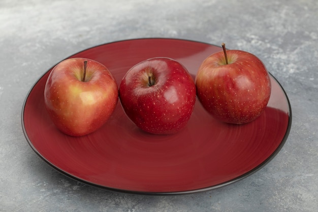 Trzy świeże dojrzałe jabłka czerwone na czerwonym talerzu.