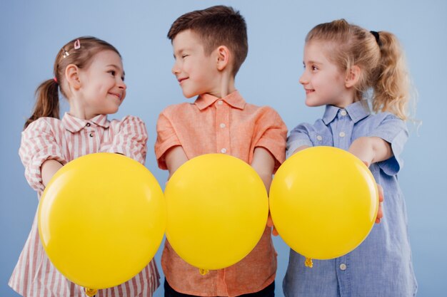 Trzy Szczęśliwe Dzieci Dziewczyny I Chłopiec Z żółtymi Balonami Z Uśmiechem Na Niebieskim Tle C...