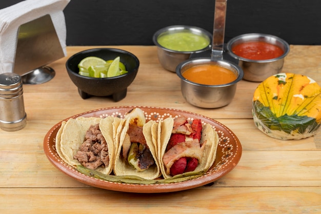 Trzy tacos podane na glinianym talerzu w towarzystwie salsy i cytryn na drewnianym stole