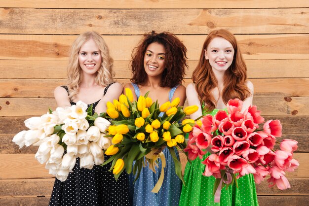 Trzy uśmiechniętej kobiety pokazuje bukiety kwiaty przy kamerą