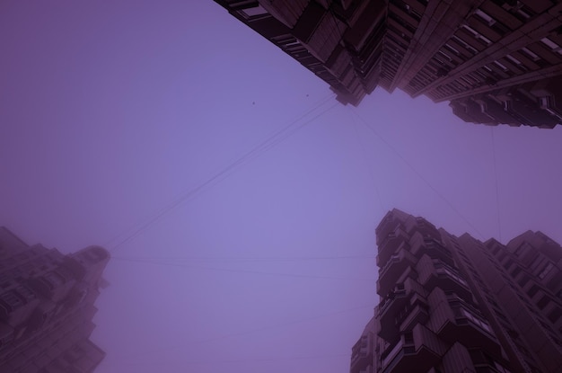 Trzy wysokie budynki mieszkalne zanurzone w mglistym, fioletowym niebie Cyberpunkowa stylistyka