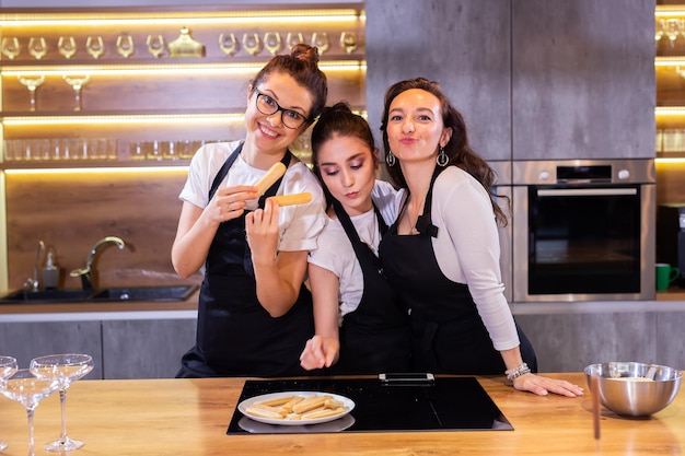 Trzy zabawne szefowej kuchni w mundurze, trzymając ciasteczka, uśmiechając się i bawiąc się przed kamerą w kuchni