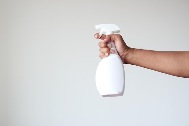 Trzymając białą butelkę ze środkiem dezynfekującym do białej ściany