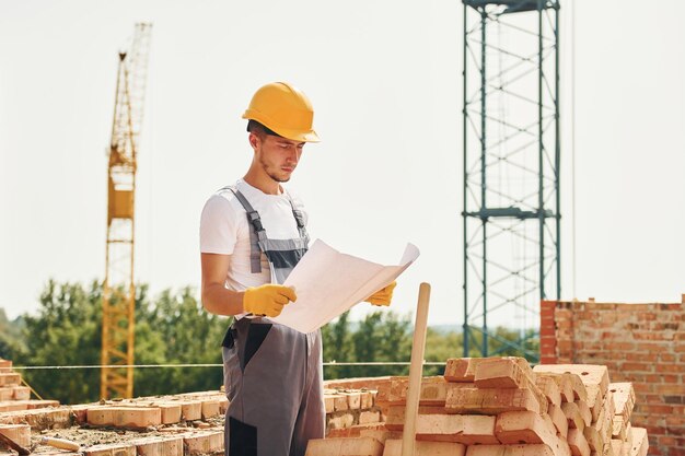 Trzymając dokument Młody pracownik budowlany w mundurze jest zajęty w niedokończonym budynku