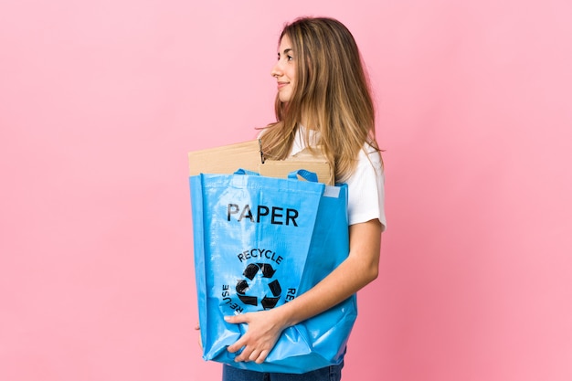 Trzymając papierową torbę recyklingową, aby poddać recyklingowi nad odizolowanym różowym, patrząc z boku