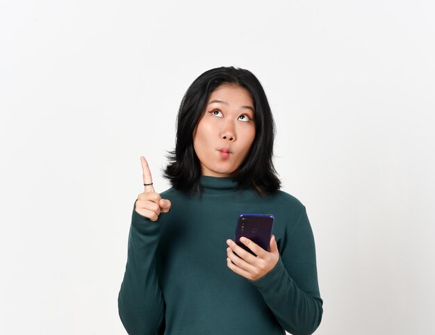 Trzymając smartfon wskazujący na piękną Azjatkę izolowaną na białym tle