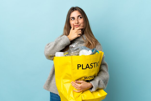 Trzymając torbę pełną plastikowych butelek do recyklingu nad odosobnionym niebieskim myśleniem, pomysł