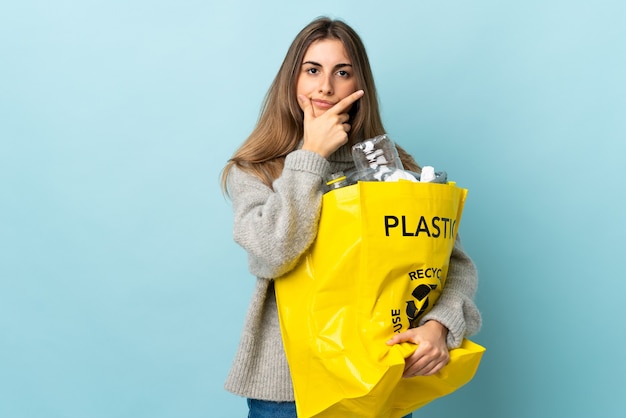 Trzymając torbę pełną plastikowych butelek do recyklingu nad odosobnionym niebieskim pomysłem