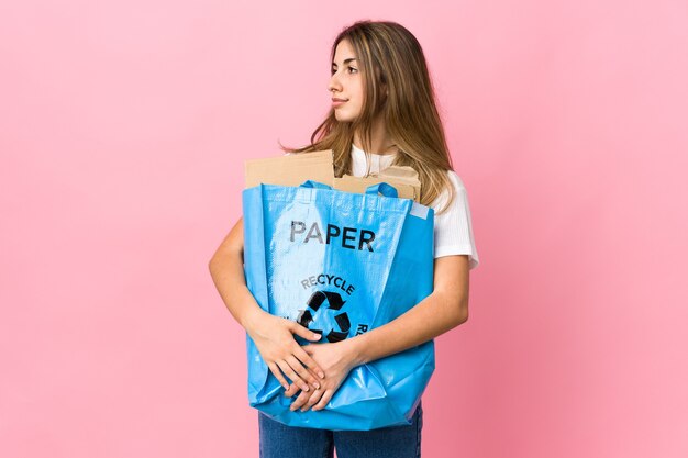 Trzymając worek do recyklingu pełen papieru do recyklingu na izolowanych różowo wyglądających bokach