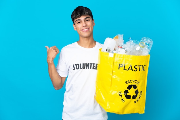 Trzymanie worka pełnego plastikowych butelek do recyklingu na niebieskiej ścianie skierowanej w bok, aby przedstawić produkt