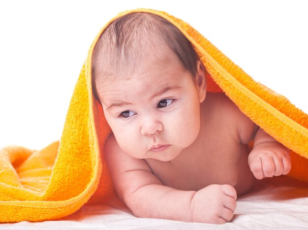 Trzymiesięczne dziecko pod pomarańczowym ręcznikiem na białym tle