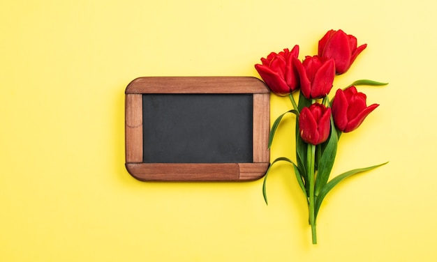 Zdjęcie tulipany czerwone na żółtym tle i tablicy kredowej. kartka okolicznościowa, zaproszenia, duże rabaty, wyprzedaże na święta.