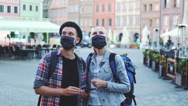 Turyści Mężczyzna I Kobieta W Maskach Ochronnych Iz Torbami Za Pomocą Smartfona. Szukają Ciekawych Atrakcji Turystycznych.