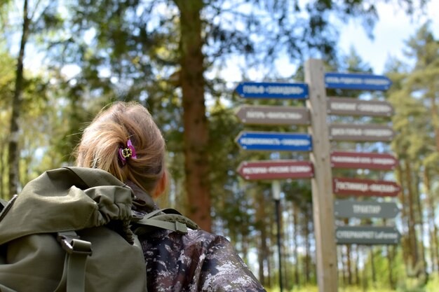 Zdjęcie turysta kobieta patrząc na drogowe drewniane znaki w lesie, szukając kierunków