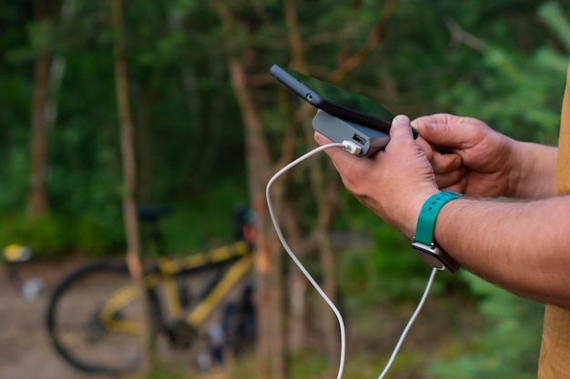 Turysta ładuje smartfon z power bankiem na tle roweru w lesie