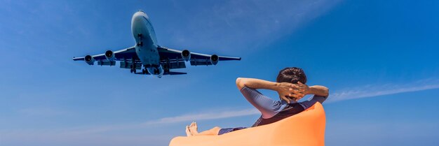Turysta mężczyzna bawi się na plaży, oglądając samoloty do lądowania podróżujące w tekście koncepcji samolotu