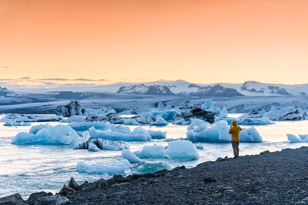 Turysta Mężczyzna W Kurtce Puchowej, Ciesząc Się Górą Lodową I łamanie Lodu O Zachodzie Słońca W Lagunie Lodowcowej Jokulsarlon, Islandia